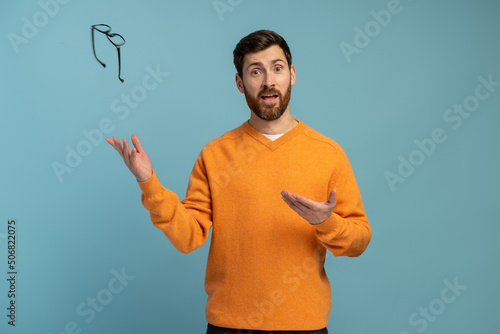Behang Young man wearing orange shirt throws glasses in trash isolated on blue background