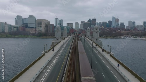 Forwards fly above Longfellow Bridge with train and cars. Cityscape with downtown buildings against cloudy sky. Boston, USA photo