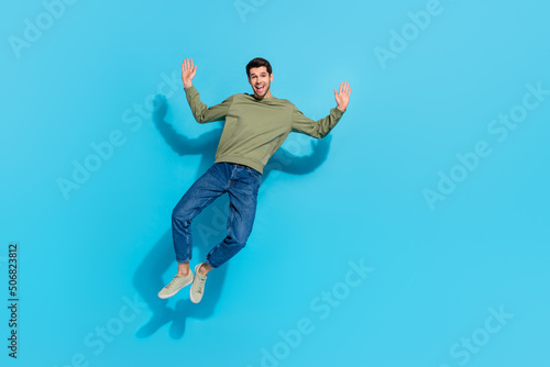 Full size photo of impressed young brunet guy jump wear shirt jeans sneakers isolated on blue background