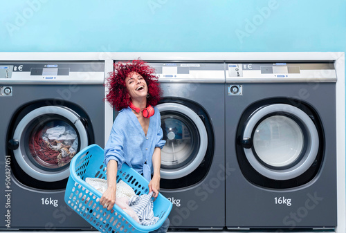 A smiling young woman with red afro hair doing laundry in a blue automatic laundromat