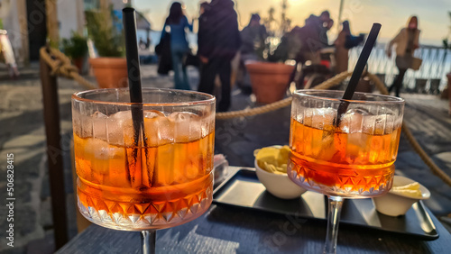 Typical Italian alcoholic aperitif (aperitivo) served in bar during sunset in the city center of Ortigia island in the city Syracuse, Sicily, Italy, Europe, EU. Aperol Spritz with ice cubes. Nut snack