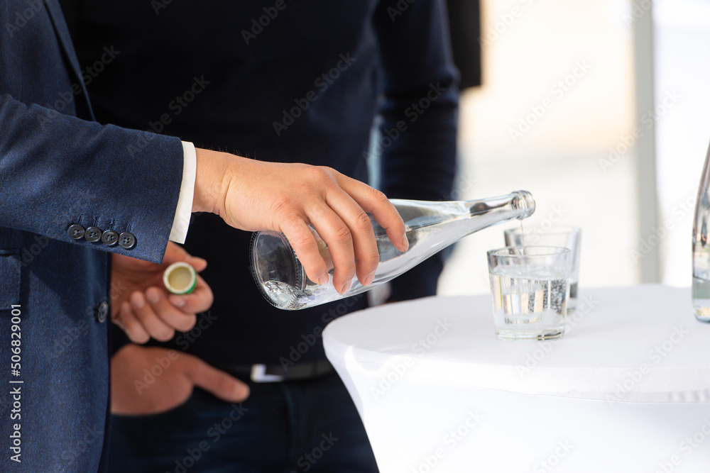 man in a suit pouring water from bottle to glass