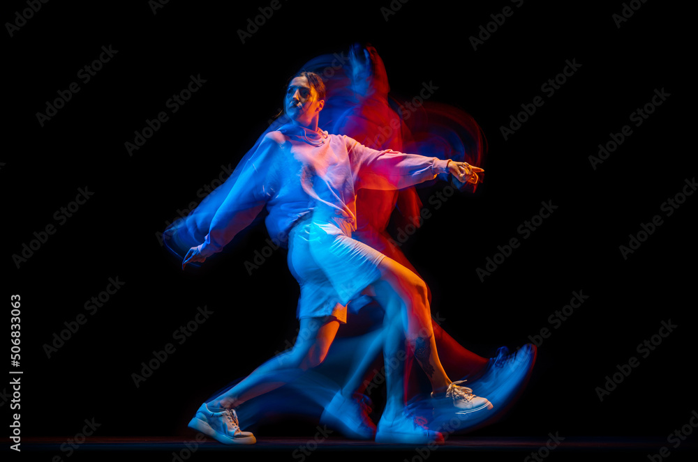 Obraz premium Young woman dancing hip-hop in sportive style clothes isolated on dark background at dance hall in mixed neon light. Youth culture, hip-hop, movement