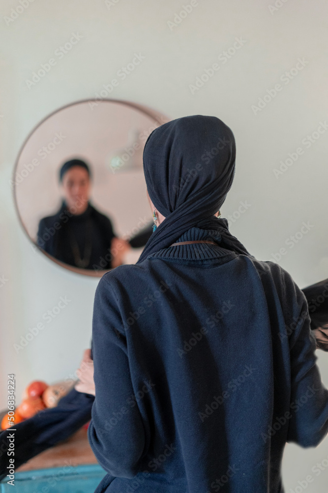 Religious Jewish woman puts a shawl on her head in front of a mirror. Back view (23)