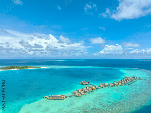 Fototapeta Naklejka Na Ścianę i Meble -  Aerial view of Maldives island, luxury water villas resort and wooden pier. Beautiful sky and ocean lagoon beach background. Summer vacation holiday and travel concept. Paradise aerial landscape pano