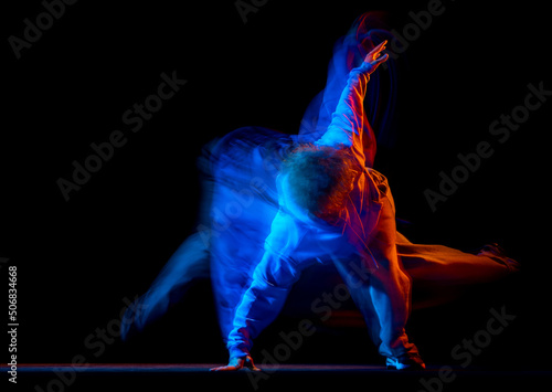 Young sportive man dancing hip-hop in sportive style clothes isolated on dark background at dance hall in mixed neon light. Youth culture, hip-hop, movement