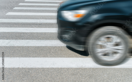 Black blurred car driving fast on crosswalk, outdoors.. Close-up, side view, selective focus on white markings of pedestrian crossing