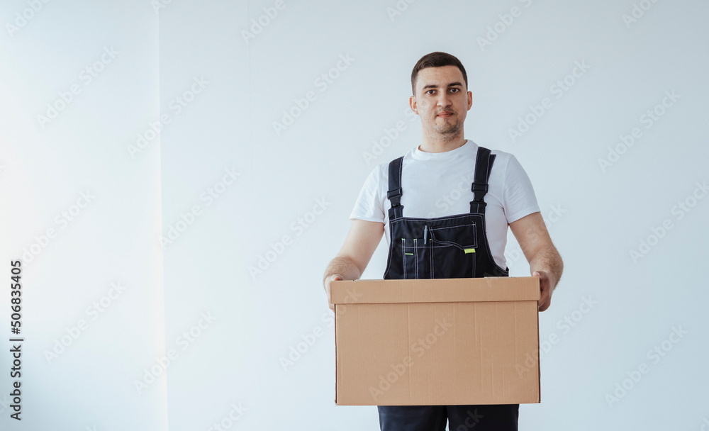 Man worker In black uniform hold big box at looking to camera. Moving to a new apartment.