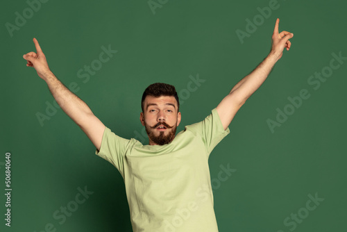 Portrait of young emotive man with funny face posing isolated over green studio background. Party time