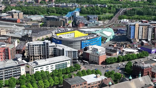 Large blue concert hall at Times Square with the railway bridges over the Tyne and the large central station Newcastle in England in the background between the green trees. Backwards drone dolly shot photo