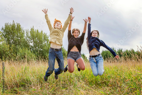 Summer holidays vacation happy people concept. Group of three friends boy and two girls jumping  dancing and having fun together outdoors. Picnic with friends on road trip in nature