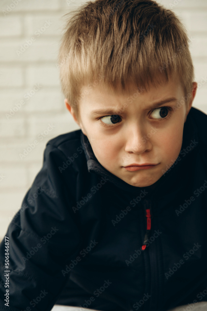 A pensive boy of 6-7 years old sits on the floor with a mysterious, cunning look. Portrait of a boy, front view A pensive boy of 6-7 years old sits on the floor with a mysterious, cunning look. Portrait of a boy, front view