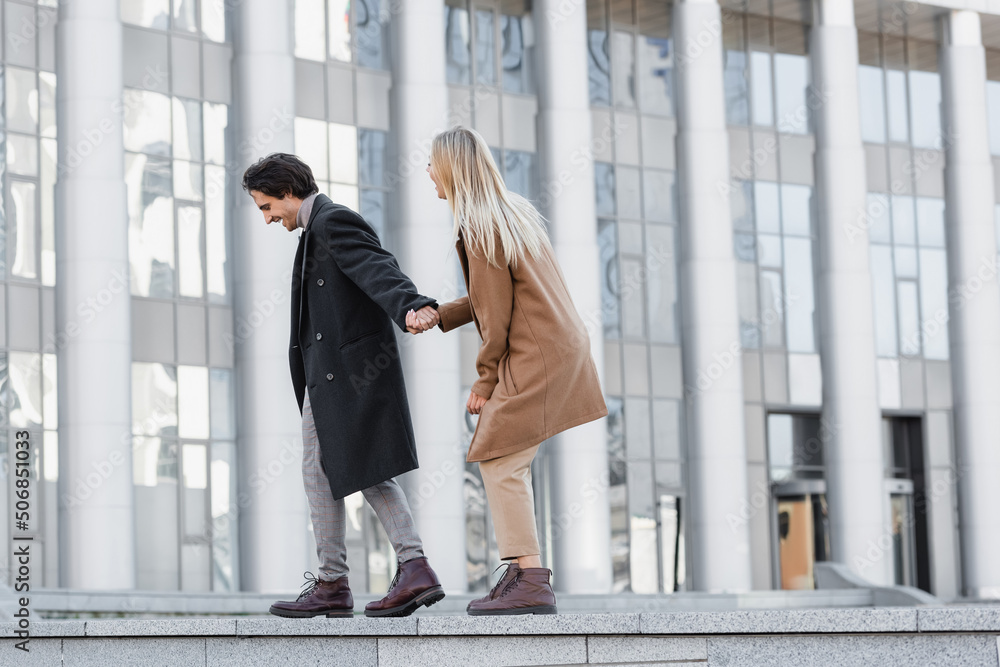 side view of excited couple in leather boots and coats holding hands and walking on parapet. side view of excited couple in leather boots and coats holding hands and walking on parapet.
