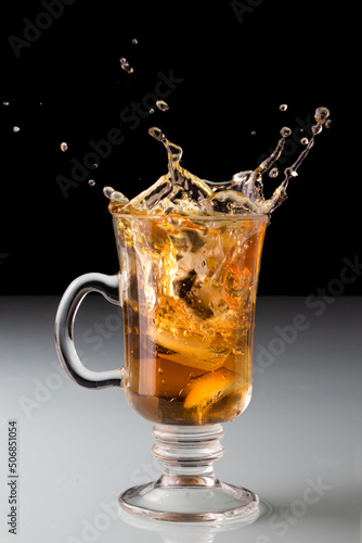 Cold tea splash on the transparent tea cup, with lemon, dark background