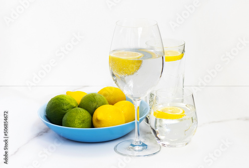 Glasses with water and lemon and a plate with lemons and lime on a white table for healthy life, energy, thermoregulation and normalization of digestion