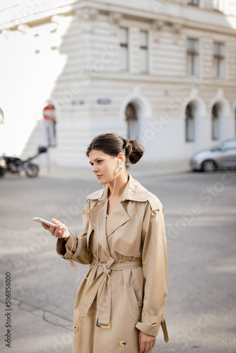 woman in wired earphones holding mobile phone and listening music on street in vienna.