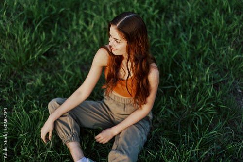 Freelance woman sitting in a park in summer on the grass looking at the sunset, sunshine in nature