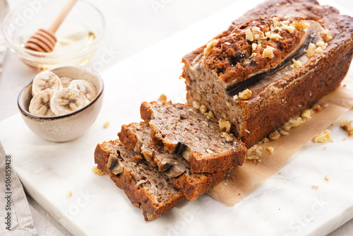 Chocolate banana bread with walnuts on a marble board and ingredients on a grey neutral background
