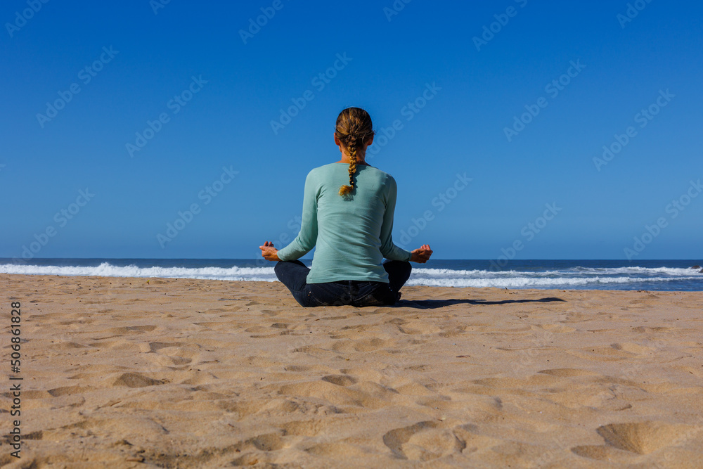 woman sitting on the beach facing east with arms open meditating