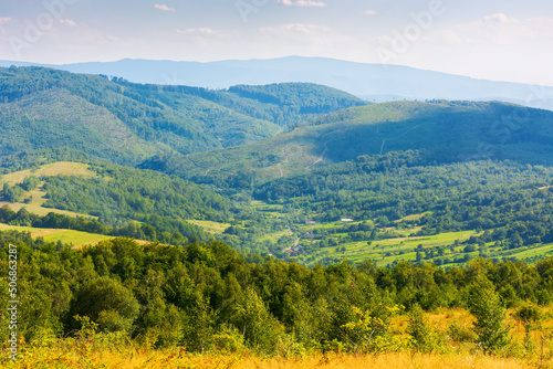 mountain scenery on an idyllic summer day. countryside landscape of capathian alps with fresh green meadows an forested hills. village in the distant valley. clouds on the blue sky in afternoon light