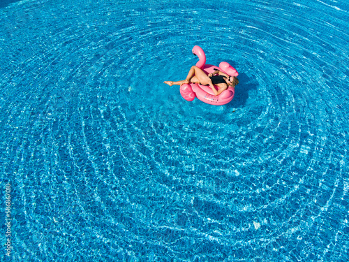 Woman on flamingo pool float in pool. Summer holidays, relaxation. Aerial drone view