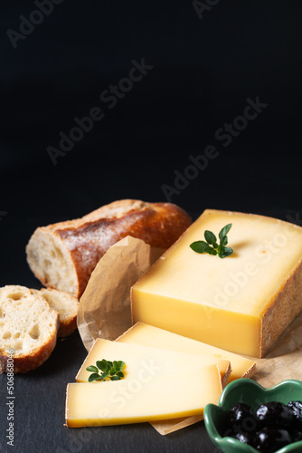 Food concept organic French Comté cheese with french bread baquette on black slate stone board with copy space