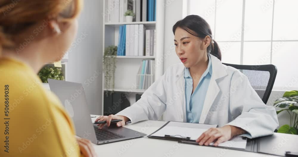 Young Asia female doctor in white medical uniform using laptop is delivering great news talk discuss results or symptoms with girl patient sitting at desk in health clinic or hospital office. Young Asia female doctor in white medical uniform using laptop is delivering great news talk discuss results or symptoms with girl patient sitting at desk in health clinic or hospital office.
