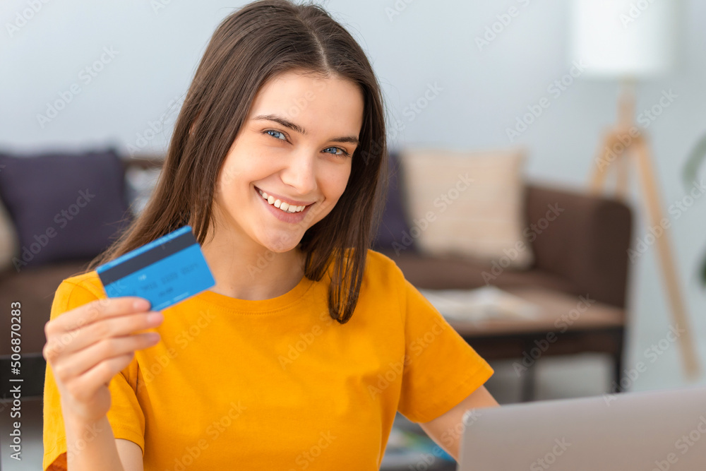 Young caucasian woman hold bank credit card, shopping online using laptop computer, buying goods or ordering online. Female holding a bank credit card in his hands and smiles friendly at the camera Young caucasian woman hold bank credit card, shopping online using laptop computer, buying goods or ordering online. Female holding a bank credit card in his hands and smiles friendly at the camera