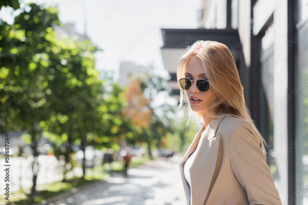 blonde woman in sunglasses looking at camera on blurred street.