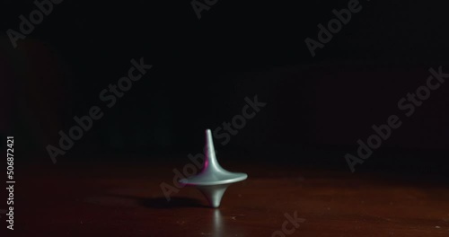 Hand playing with a top spinning on a wooden table in slow motion