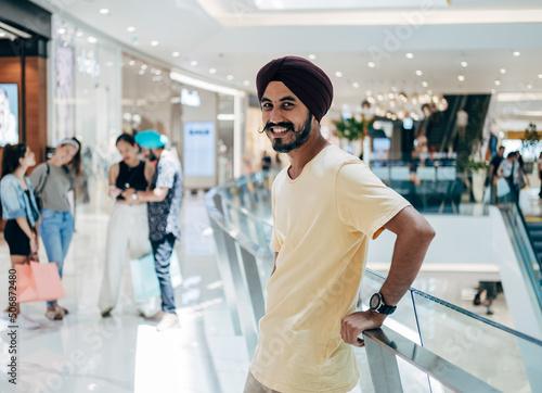 Portrait Of Happy Indian Man Leaning On A Fence In The Shopping Mall And Looking At Camera