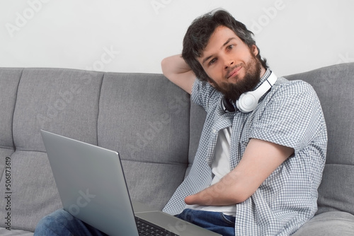 Handicapped disabled man with amputated two stump hands working on laptop at home looking at camera and smiling. Problem of adaptation to life people with disabilities. Independent Invalid person.