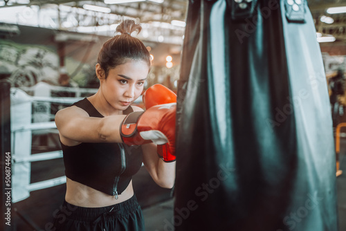 Young Asian woman wearing boxing gloves and hitting the punching bag, Young woman doing boxing training at the sport gym. © somchairakin