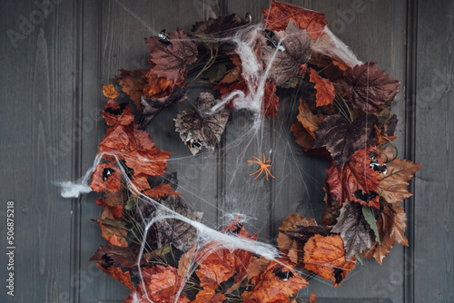 Colorful wreath for halloween hanging on wooden house door made of old orange maple leaves.Spider web.Decorating of porch.Home, outdoort,street decoration,entertainment for children,horror atmosphere photo