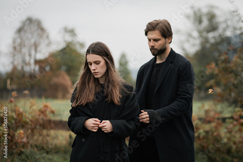A young couple in love in black coats walks in the countryside in the rain. Autumn gloomy mood. cinematic image