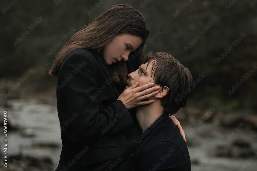 Fototapeta premium A young couple in love in black coats walks in the countryside in the rain. Autumn gloomy mood. cinematic image