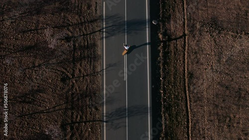 Aerial top view shot on man cruising on longboard on empty asphalt road. Surfskate surfing experience, taking turns and curves with skateboard. Freedom lifestyle, summer experience photo
