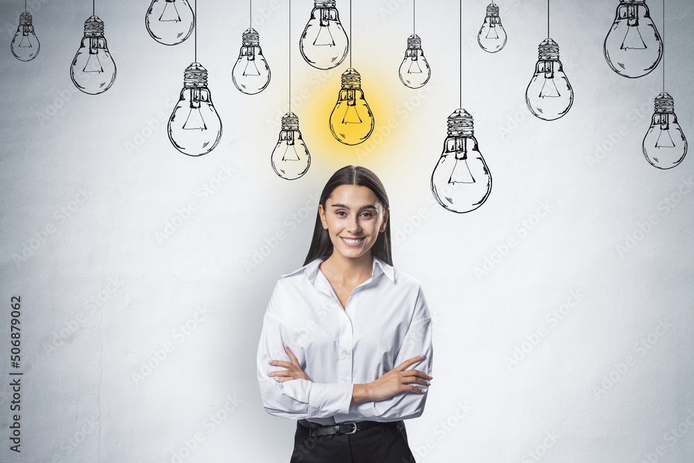 Creative idea and startup concept with happy and smiling young woman in white shirt at light wall background with hand drawn white lightbulbs and yellow one switched on - obrazy, fototapety, plakaty 