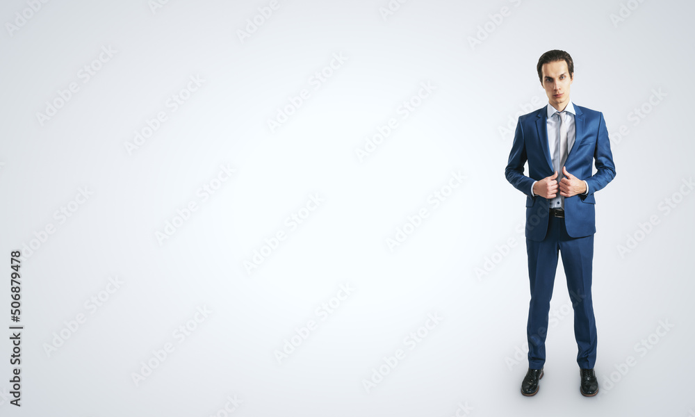 Young self-confident businessman in blue suit and grey tie isolated on light grey wall background with blank place for your logo, mockup Young self-confident businessman in blue suit and grey tie isolated on light grey wall background with blank place for your logo, mockup