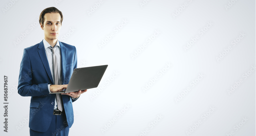 Young businessman in blue suit working with modern laptop, isolated on light grey wall background, with blank place for you text or logo, mockup Young businessman in blue suit working with modern laptop, isolated on light grey wall background, with blank place for you text or logo, mockup