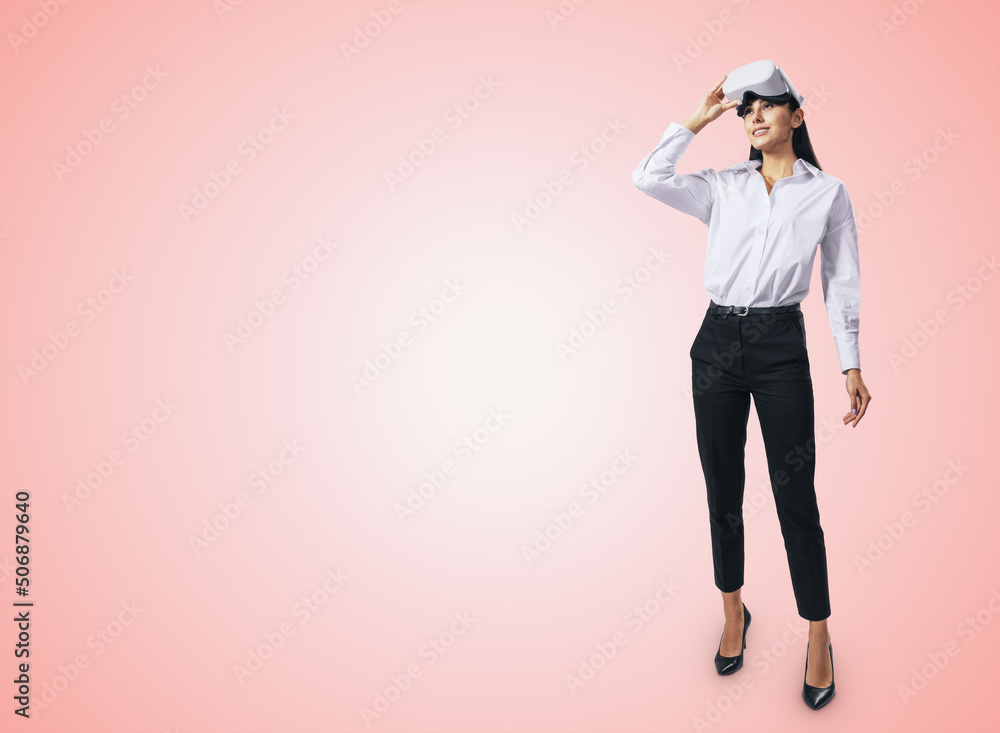 Virtual reality concept with stands at full length young woman looking up and white VR headset on her head on abstract light pink background with place for your logo or text, mockup Virtual reality concept with stands at full length young woman looking up and white VR headset on her head on abstract light pink background with place for your logo or text, mockup