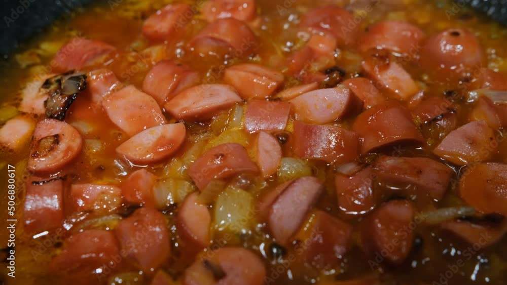 Ingredients for soup, sliced onion and sausages fried in tomato sauce in a black pan. Ingredients for soup, sliced onion and sausages fried in tomato sauce in a black pan.