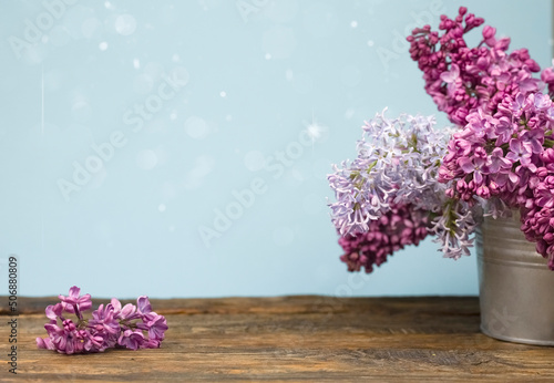 A bouquet of lilacs in an iron bucket on a dark wooden background, highlights, blurry lights and copy space. A branch of purple lilac on a wooden table.