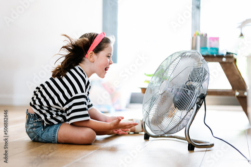 Little girl at home sitting on the floor playing with fan photo