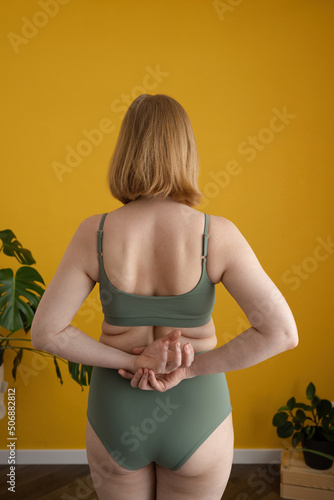 Anonymous curvy lady holding hands behind back while standing near yellow wall