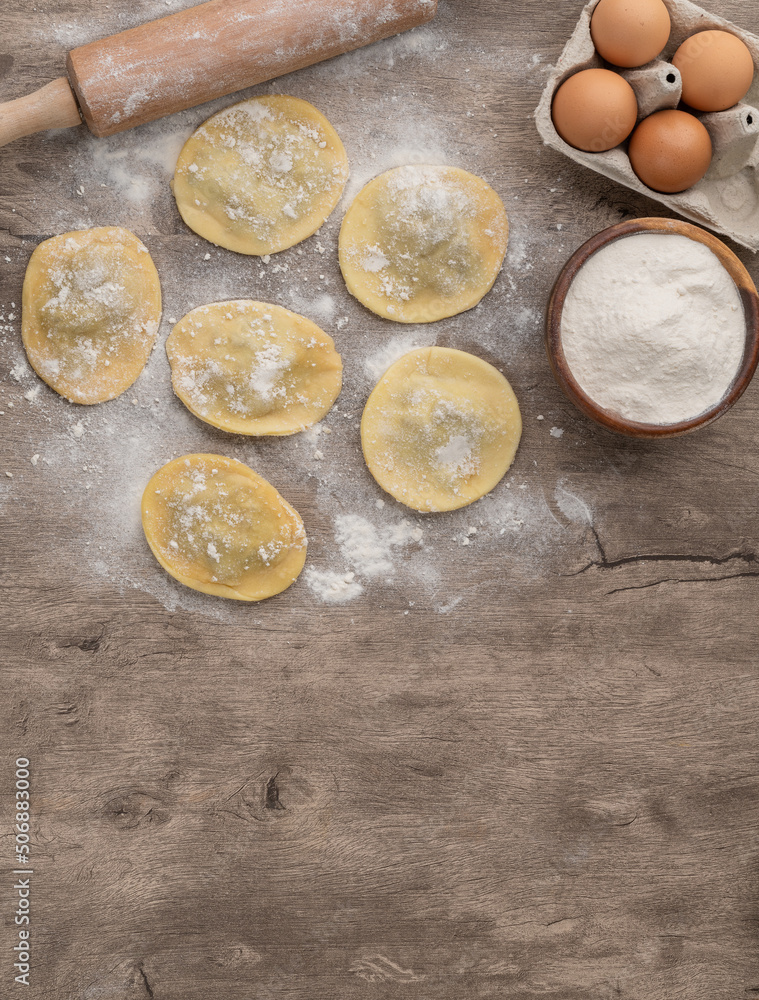 Uncooked stuffed raviolonis or raviolis with flour and ingredients over wooden table with copy space Uncooked stuffed raviolonis or raviolis with flour and ingredients over wooden table with copy space