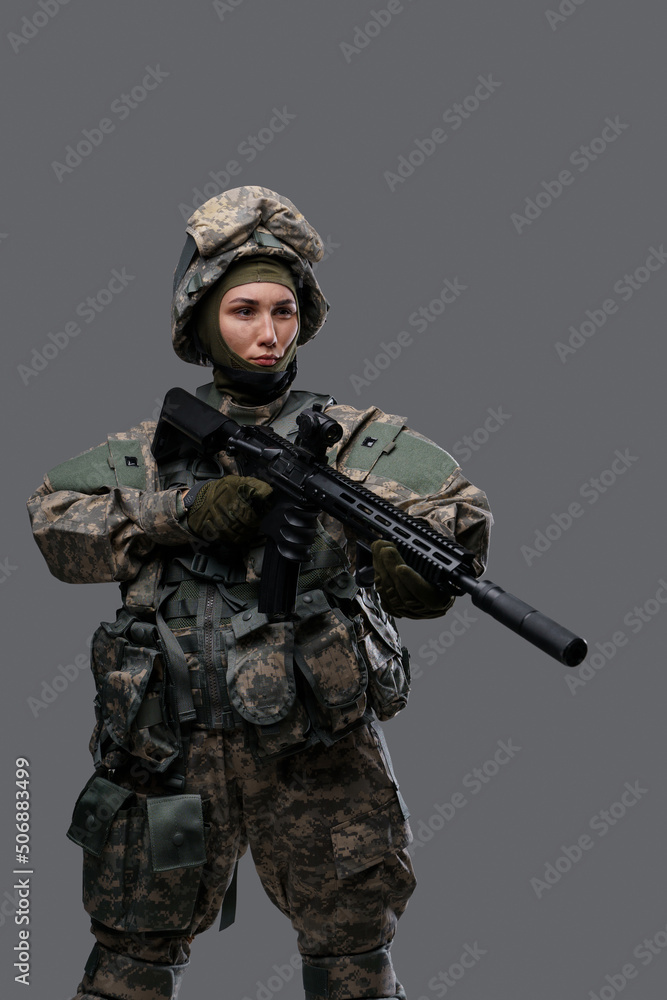 Studio shot of military woman dressed in camouflage clothes and helmet holding rifle.