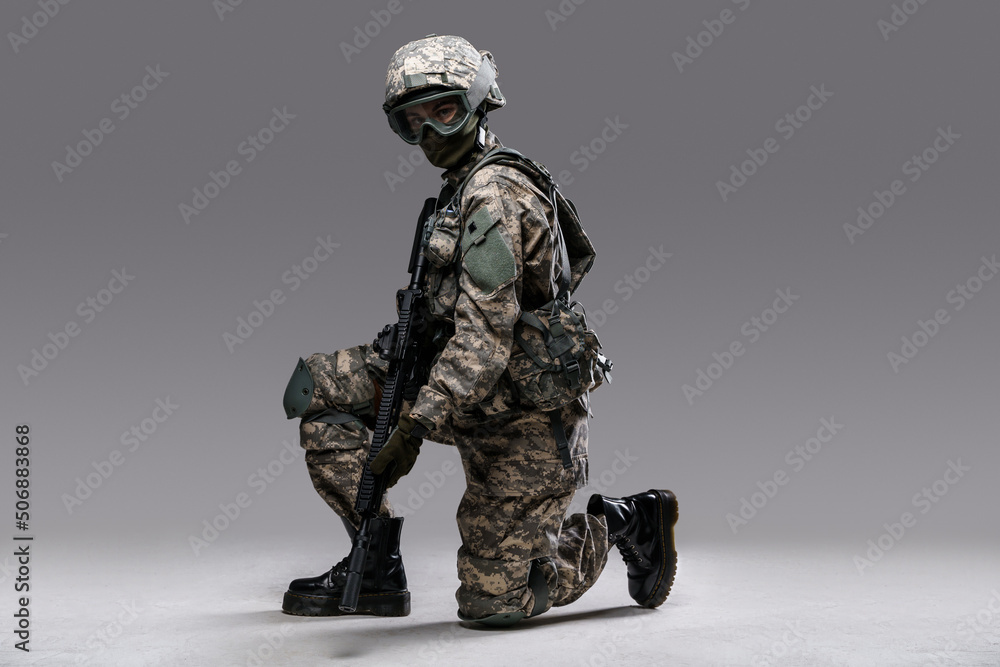 Portrait of soldier woman with rifle sitting on her knee isolated on grey background. Portrait of soldier woman with rifle sitting on her knee isolated on grey background.