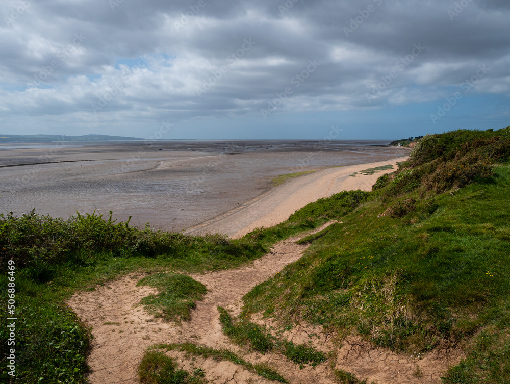 A clifftop view from the Wirral Country Park at Thurstaston looking down to the beach and across the Dee Estuary, at low tide, to the North Wales coast. Cloudy sky. A clifftop view from the Wirral Country Park at Thurstaston looking down to the beach and across the Dee Estuary, at low tide, to the North Wales coast. Cloudy sky.