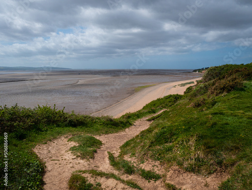 A clifftop view from the Wirral Country Park at Thurstaston looking down to the beach and across the Dee Estuary, at low tide, to the North Wales coast. Cloudy sky.